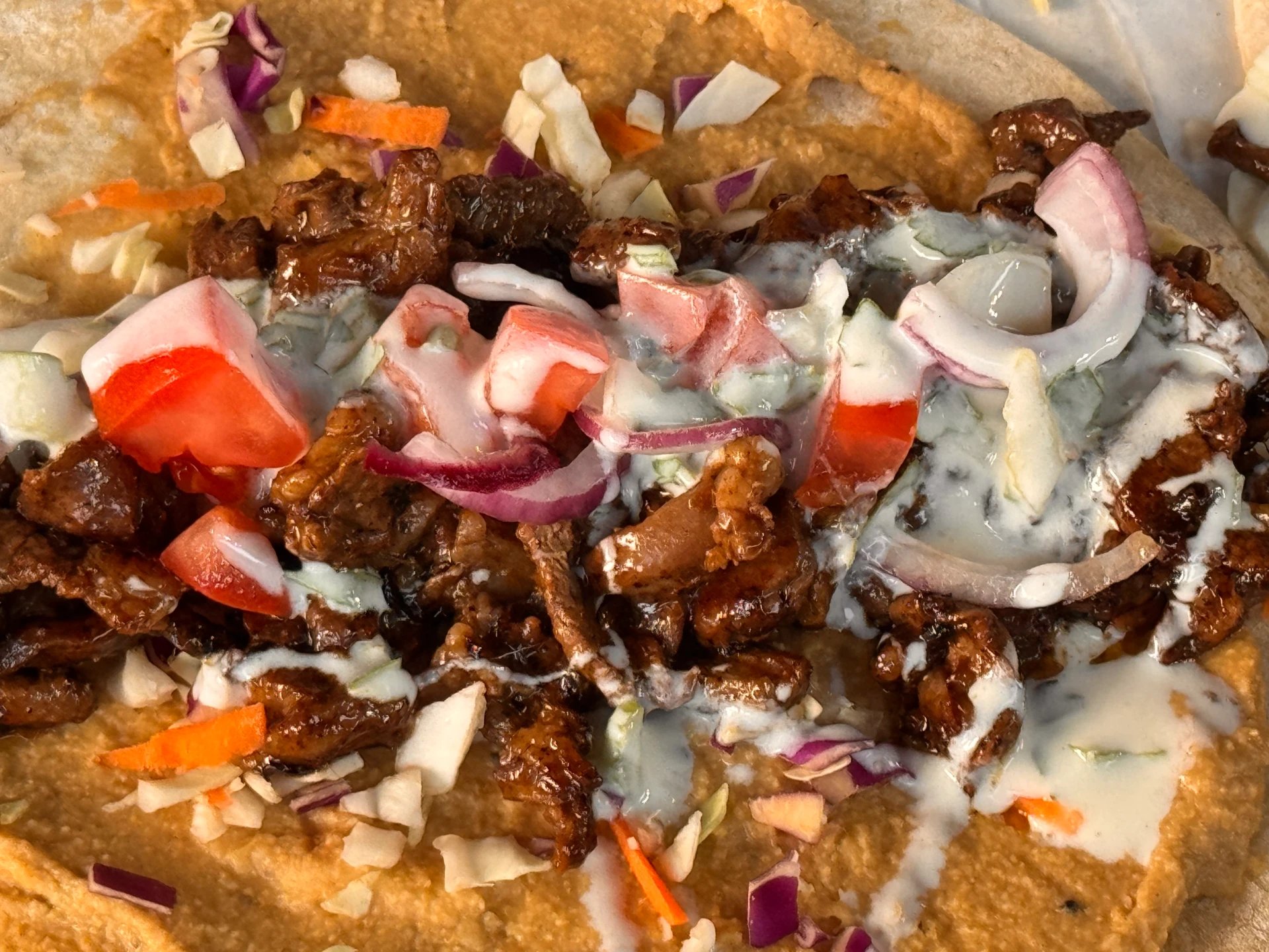 A Hestia shawarma wrap with hummus, tomato, red onion and garlic sauce